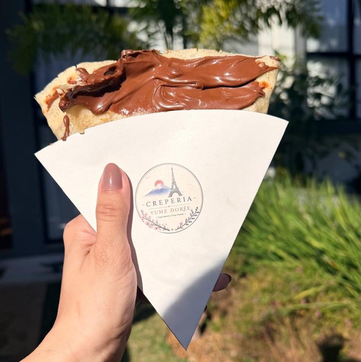 Mão segurando cone com chocolate e o logo da Creperia Yume Dorée